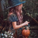 woman in black hat and brown dress holding pumpkin