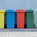 four assorted-color trash bins beside gray wall